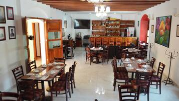 A dining area with multiple tables and chairs, a bar area with shelves of bottles, and a television mounted on the wall.