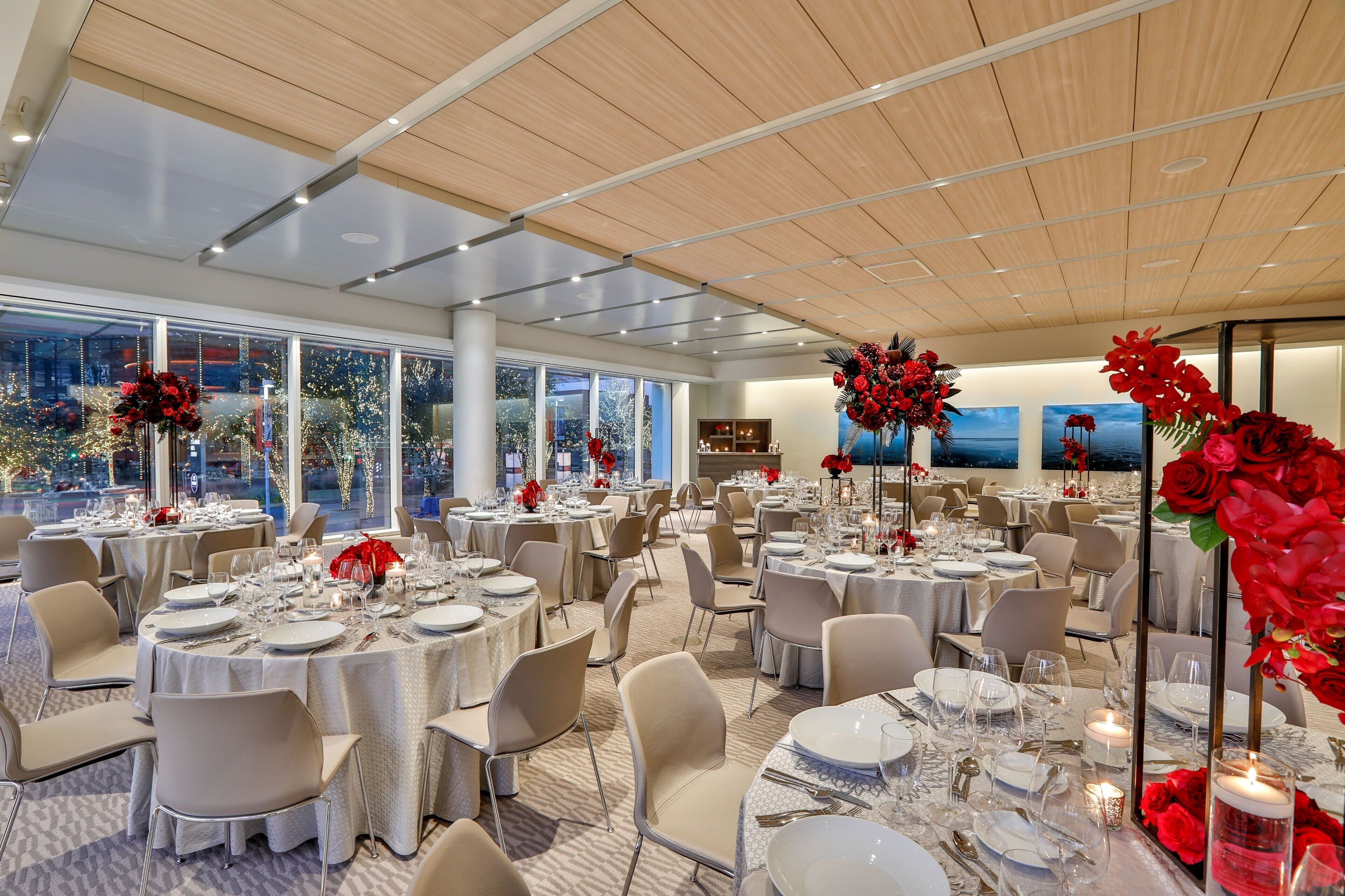 A spacious banquet hall with round tables set for dining, large windows offering a view of the city, and elegant floral centerpieces.