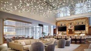 A spacious lounge area with sofas and armchairs, a bar with shelves of bottles, and a large TV screen. - HALL Arts Hotel, Dallas, Autograph Collection (Dallas)