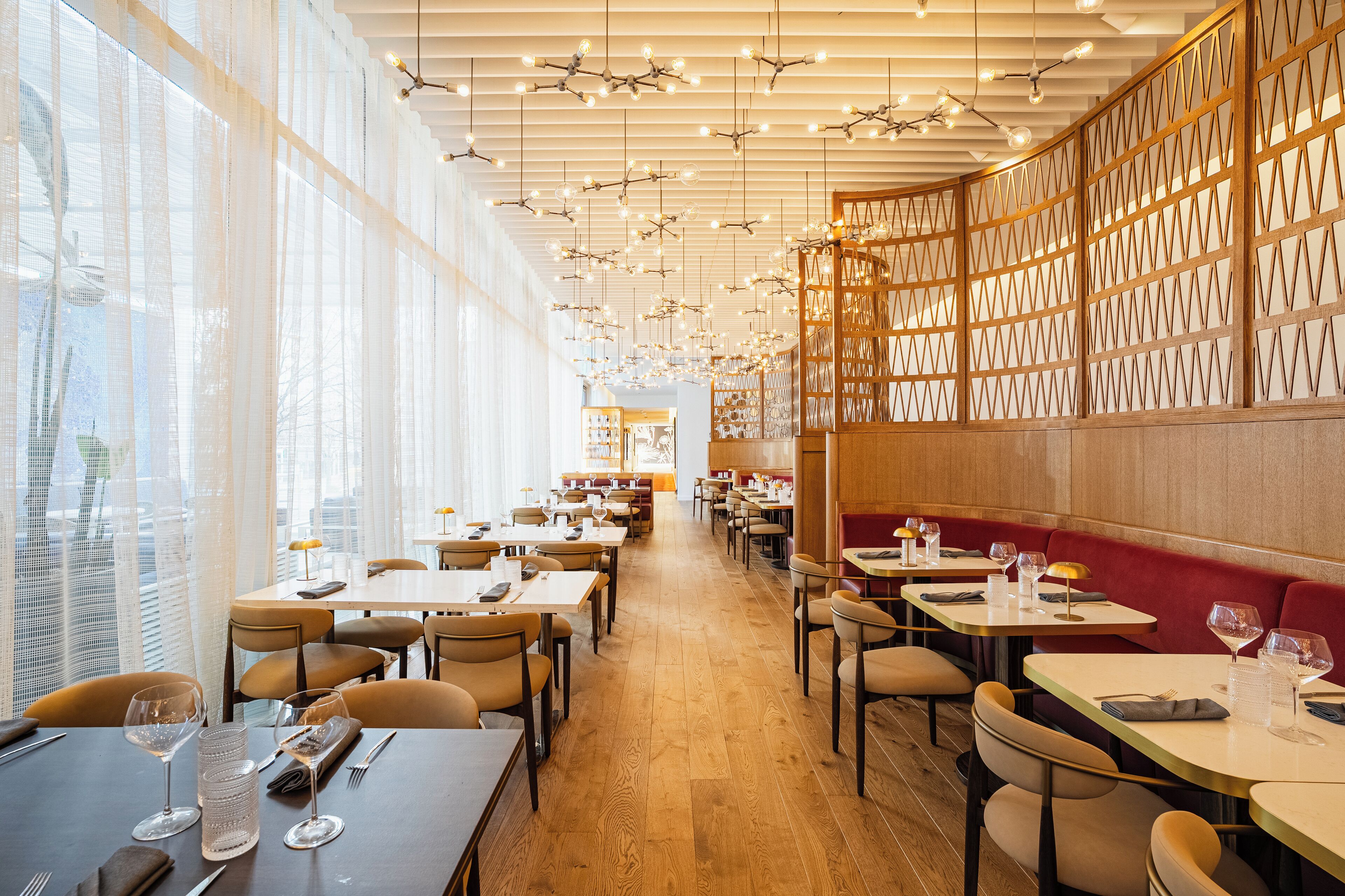 A modern restaurant with wooden floors, tables with chairs, and hanging lights.