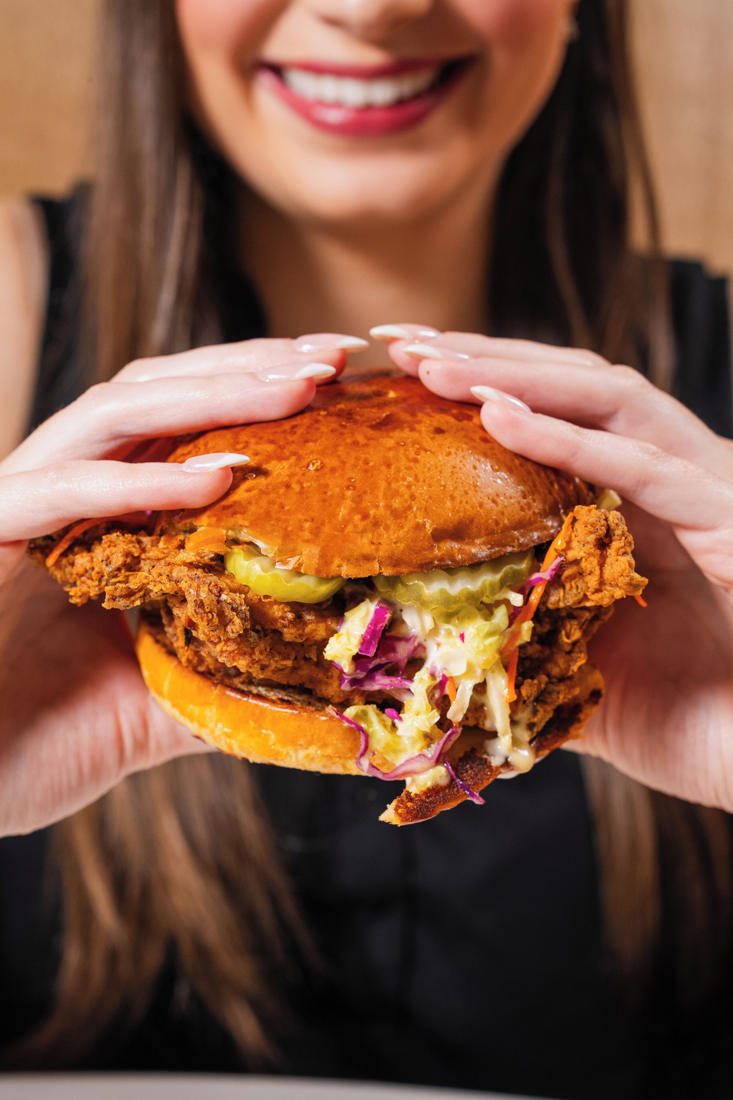 A person holding a sandwich with visible layers of meat, lettuce, and a bun.