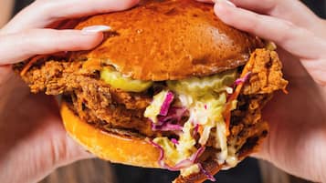 A person holding a sandwich with visible layers of meat, lettuce, and a bun.