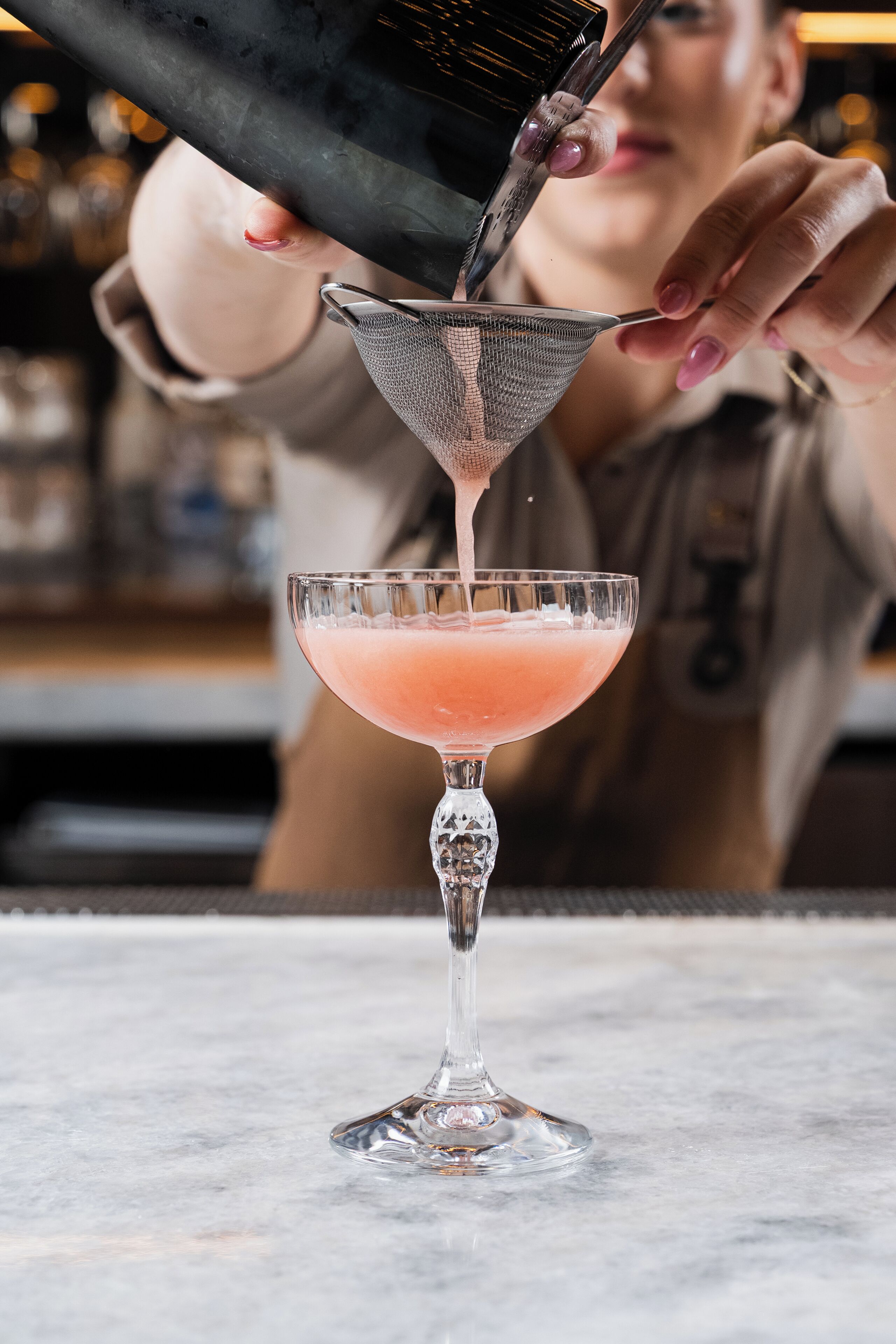 En bartender häller en rosa vätska i ett martiniglas.