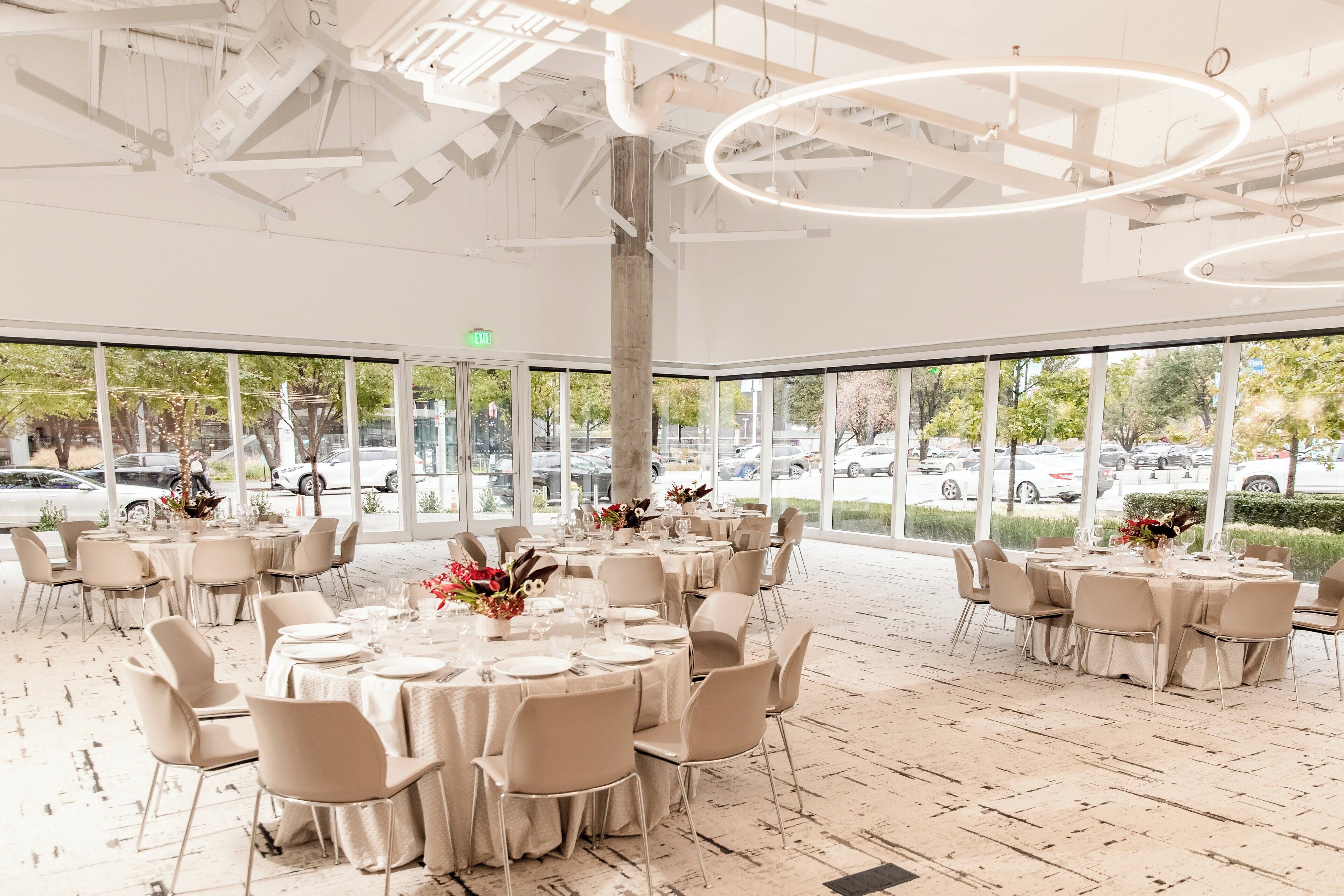 A spacious indoor dining area with round tables and chairs, large windows, and a modern ceiling design.