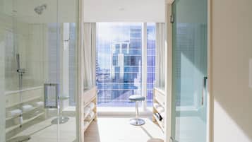 A modern bathroom with a glass shower enclosure, a vanity with a mirror, and a view of a cityscape through large windows.