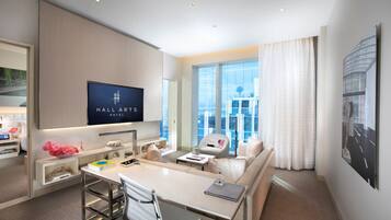 Una habitación de hotel moderna con comedor, sofá, televisión y un amplio ventanal con vista a la ciudad.