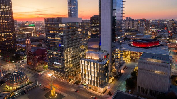 A high-rise building with a modern glass facade, surrounded by other skyscrapers and a circular plaza with a red-lit structure. - HALL Arts Hotel, Dallas, Autograph Collection (Dallas)