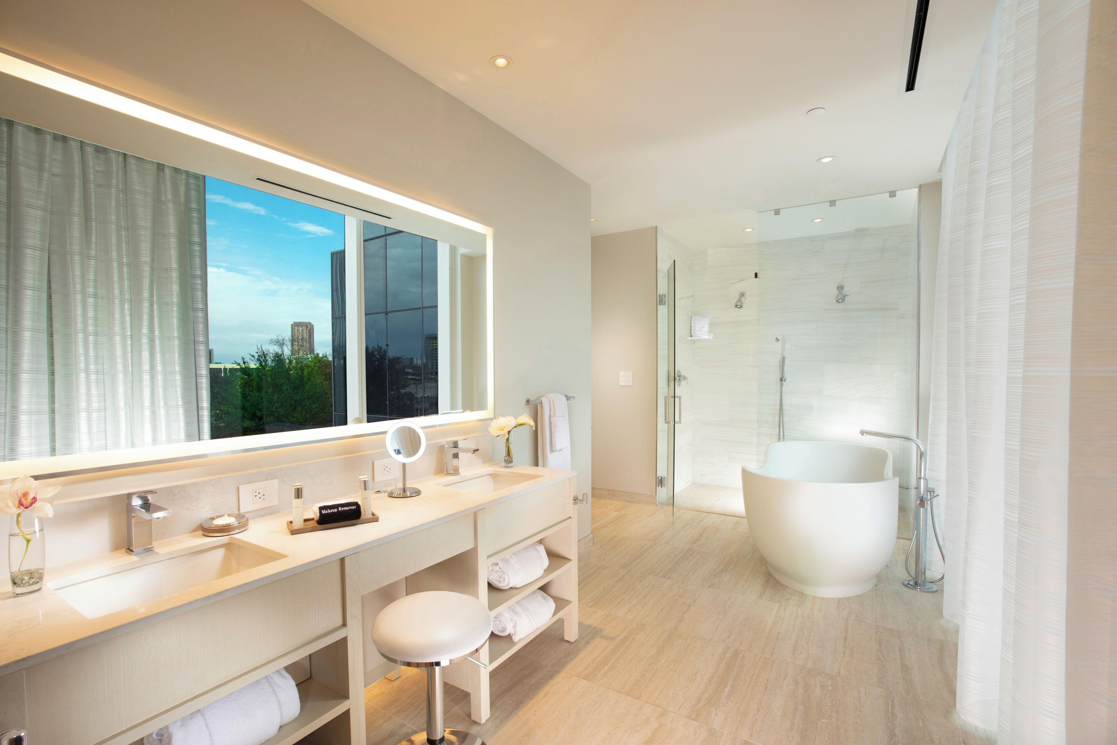 A modern bathroom with a large mirror, vanity, bathtub, and glass shower enclosure.