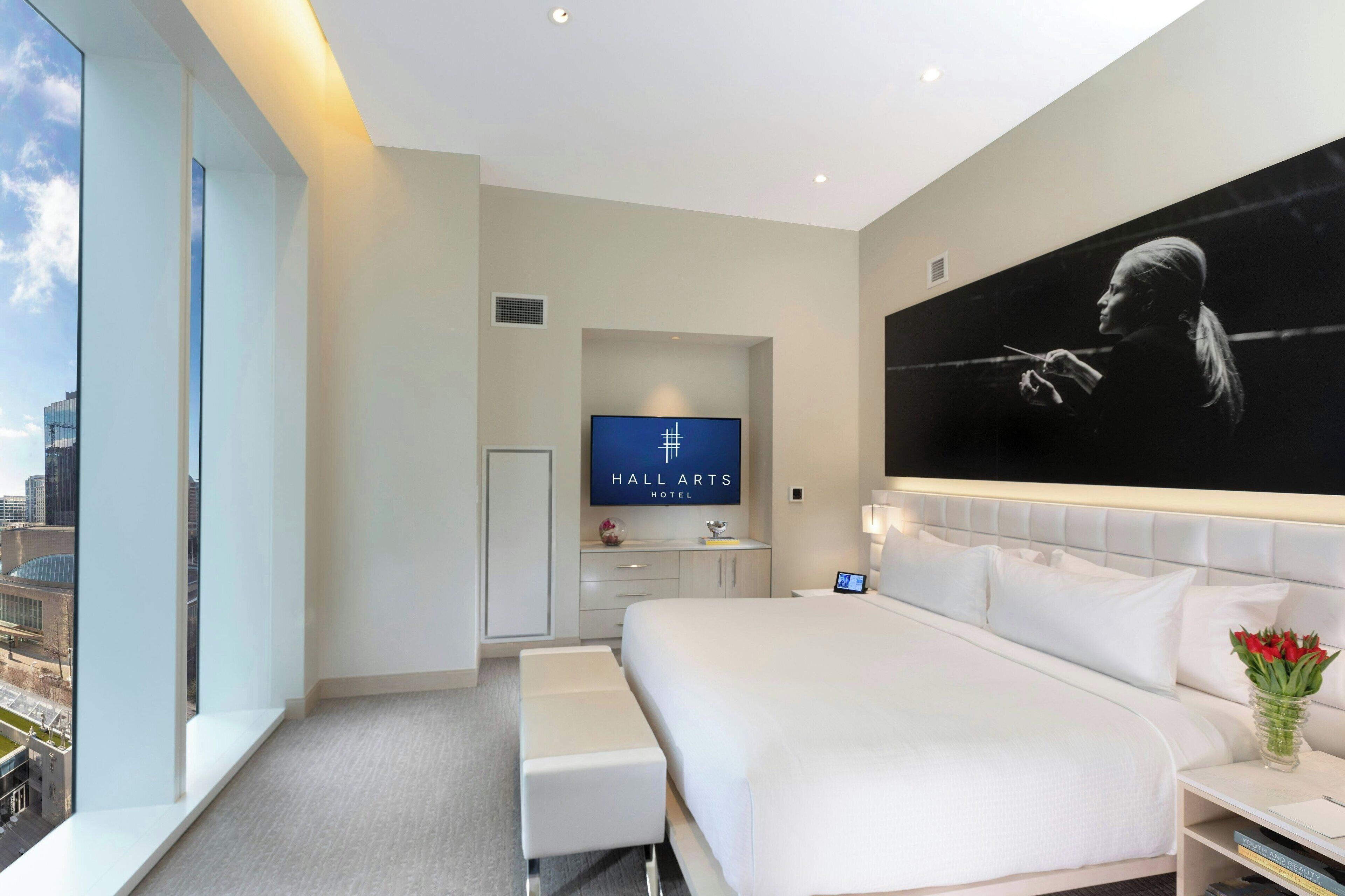 A modern hotel room with a large bed, a seating area, a flat-screen TV, and a city view.