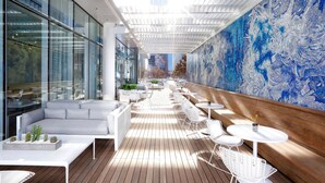 A modern outdoor seating area with white furniture, a wooden floor, and a large blue abstract mural on the wall. - HALL Arts Hotel, Dallas, Autograph Collection (Dallas)