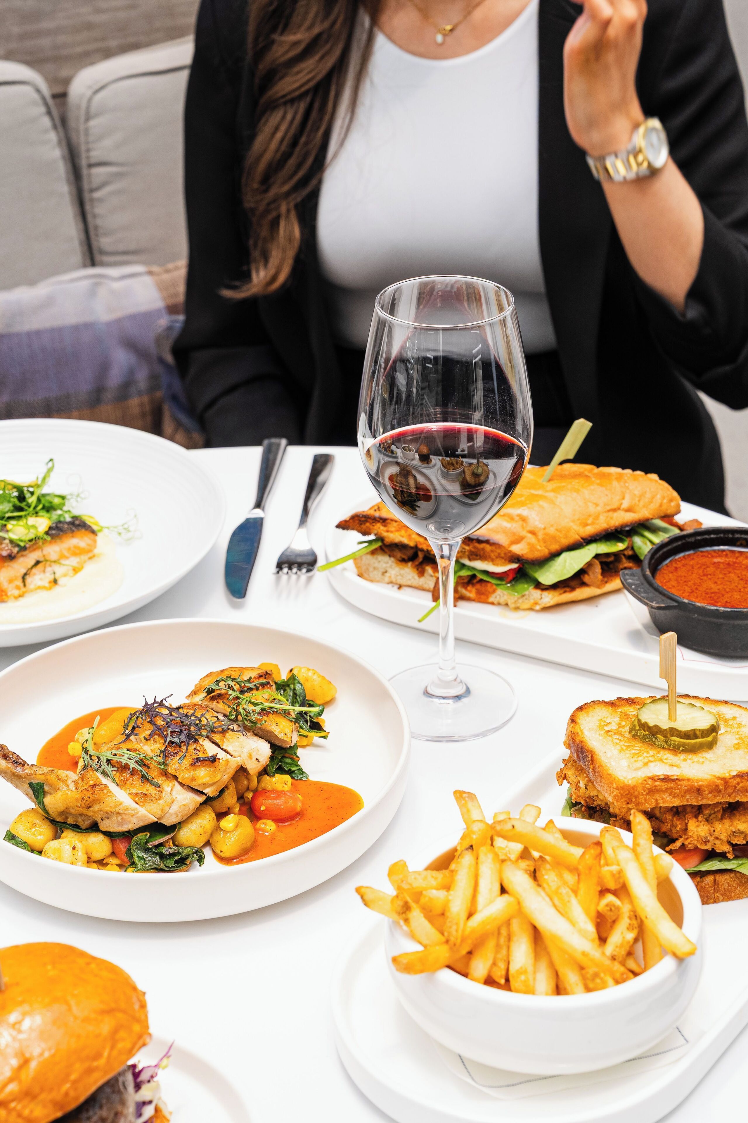A dining table with various dishes, including a sandwich, fries, and a glass of red wine.