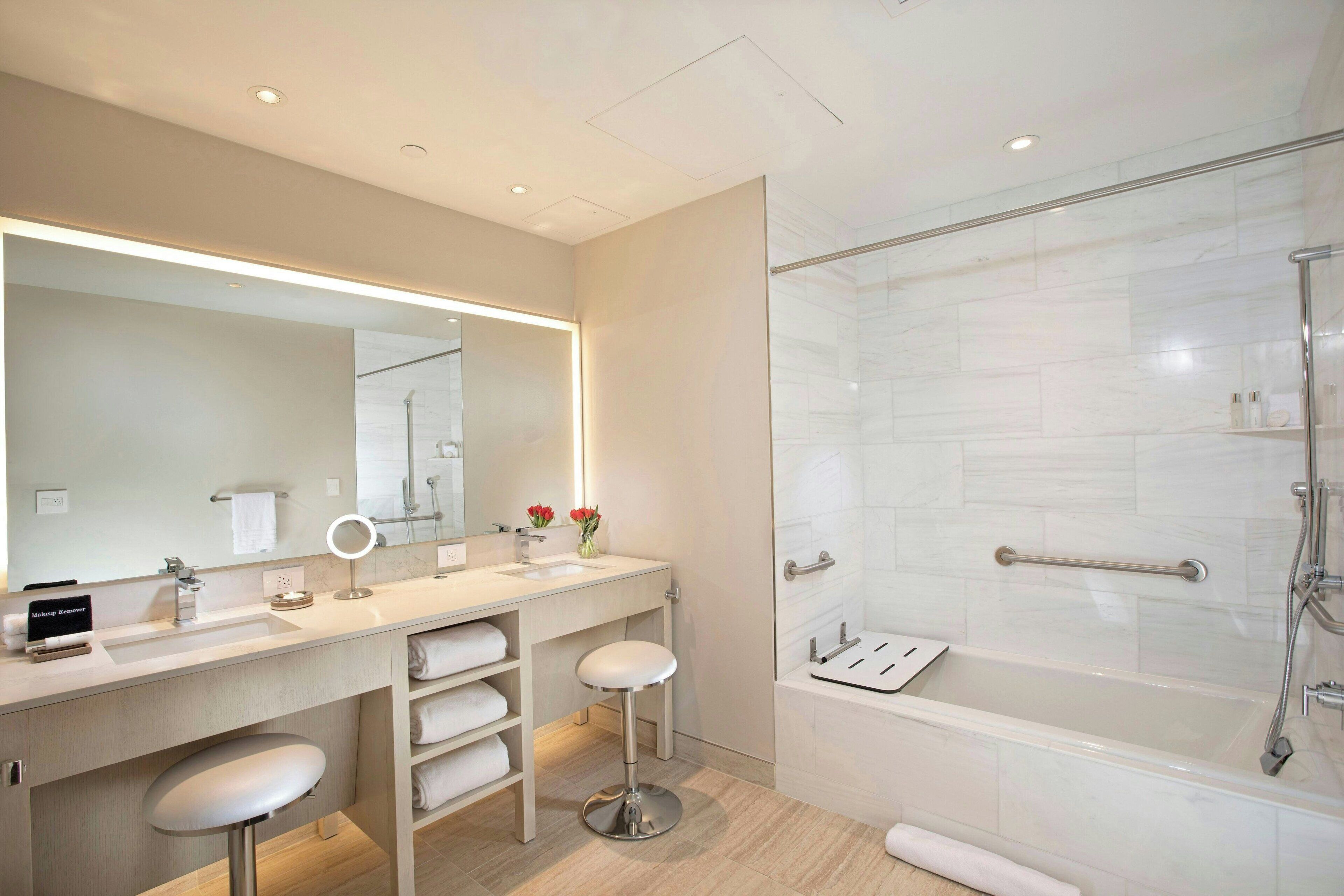 A modern bathroom with a large mirror, two sinks, a vanity, and a glass-enclosed shower area.