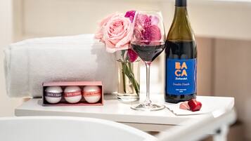 A neatly arranged table with a bottle of wine, a glass, a box of honey bath products, a towel, and a vase with flowers.