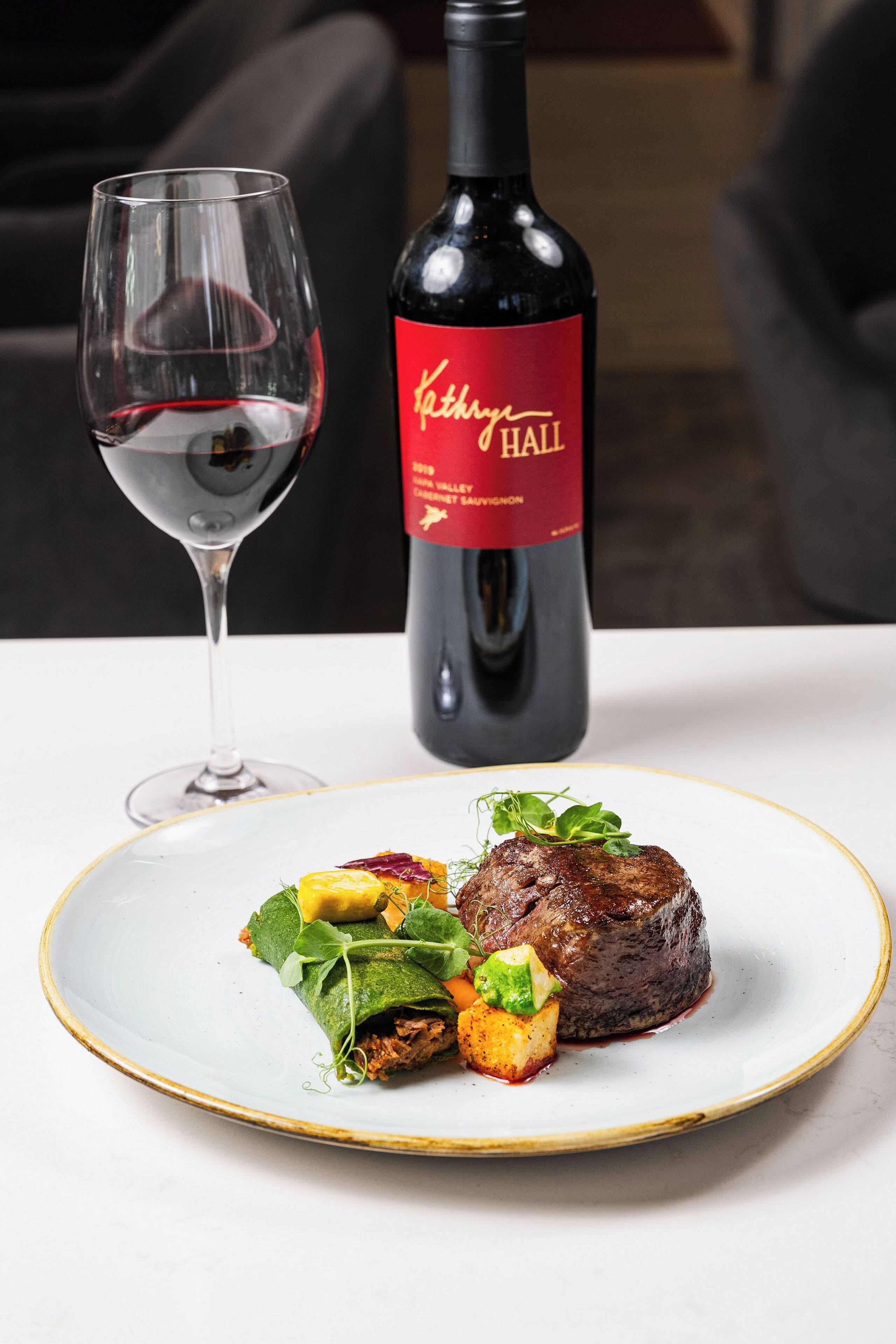 Ein Teller mit Steak und Gemüse, ein Weinglas und eine Weinflasche auf einem Tisch.