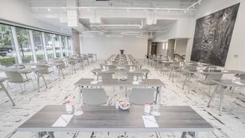 A spacious conference room with long tables, chairs, and a large abstract painting on the wall.