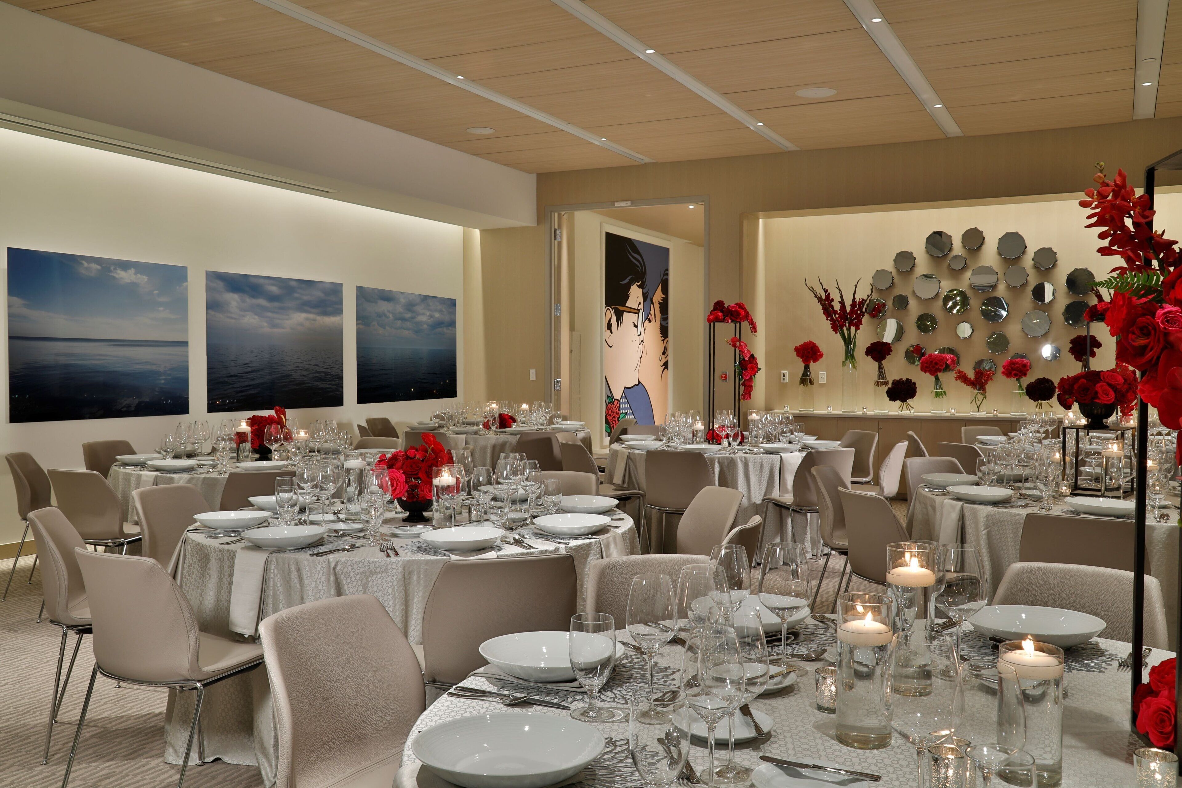 A well-lit dining area with round tables set for a meal, featuring white tablecloths, glassware, and candles.