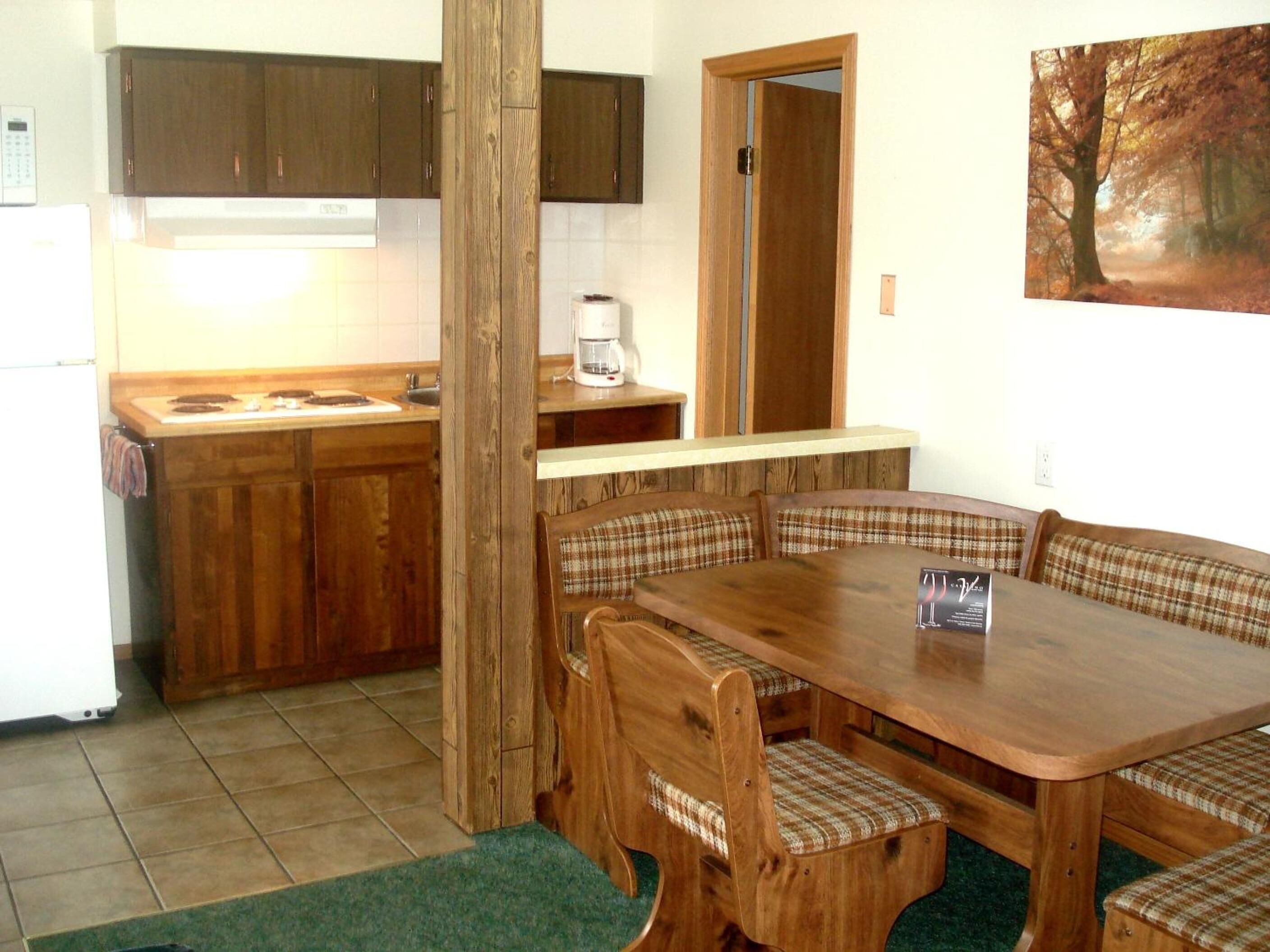 Una cocina con armarios de madera, una cafetera y una mesa de comedor con bancos.