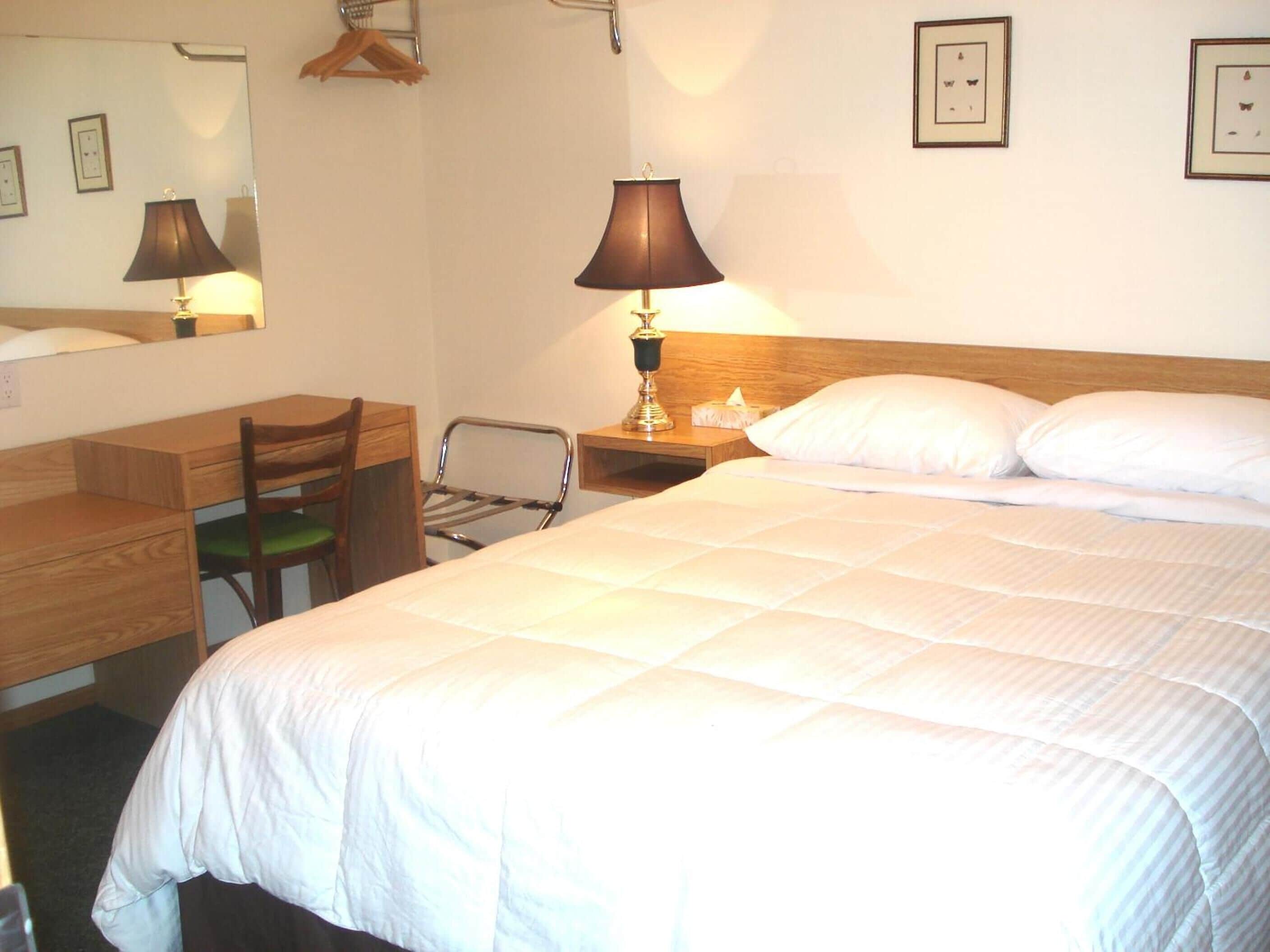 Ett hotellrum med en säng, ett skrivbord, en stol, en lampa och en spegel.