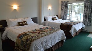 Two single beds with white linens, a quilt, and a headboard. There are wall-mounted lights and a window with curtains. - Motel Tyrol (Radium Hot Springs)