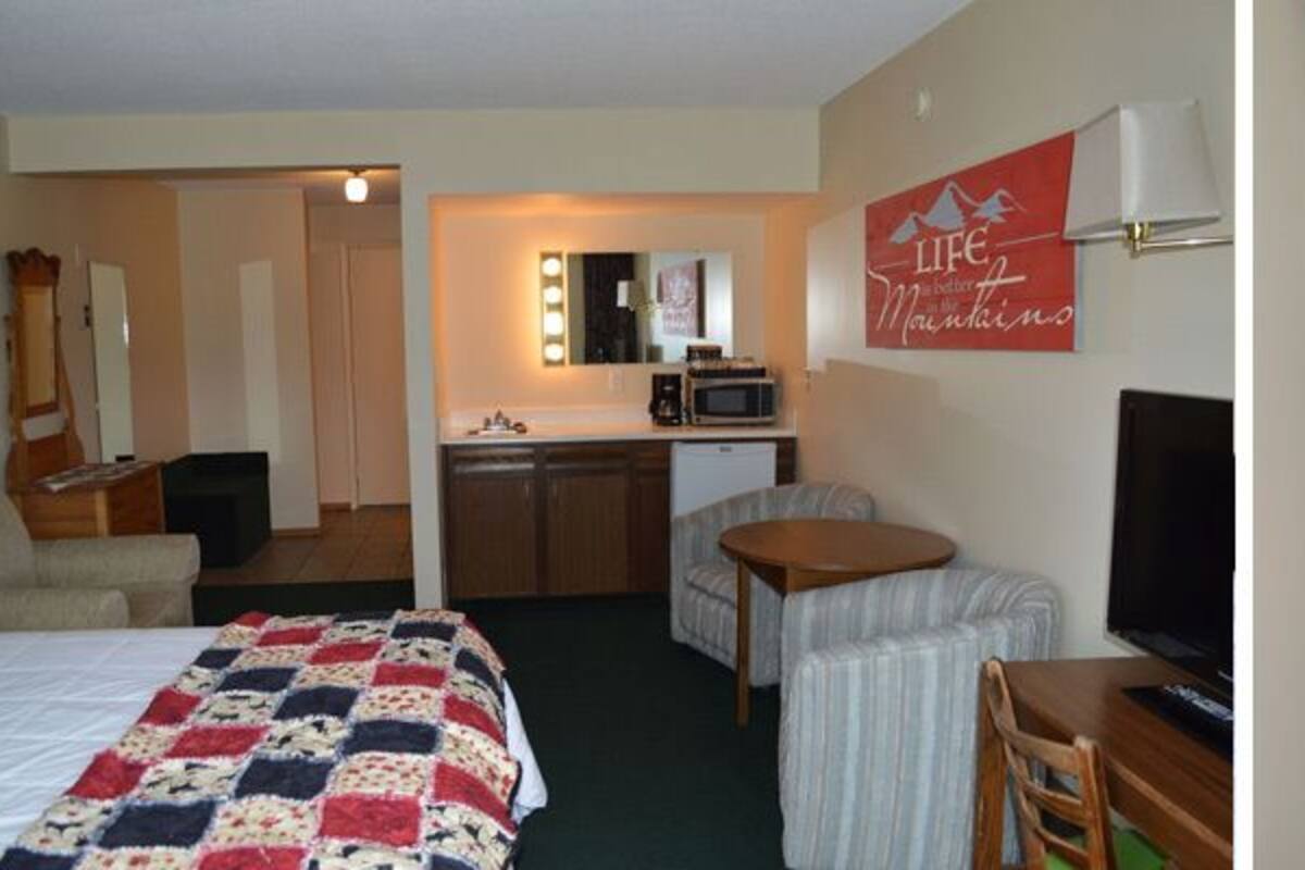 Ein Hotelzimmer mit einem Bett, einem Schreibtisch mit Computer, einem Sessel, einer Kommode und einem Fernseher.