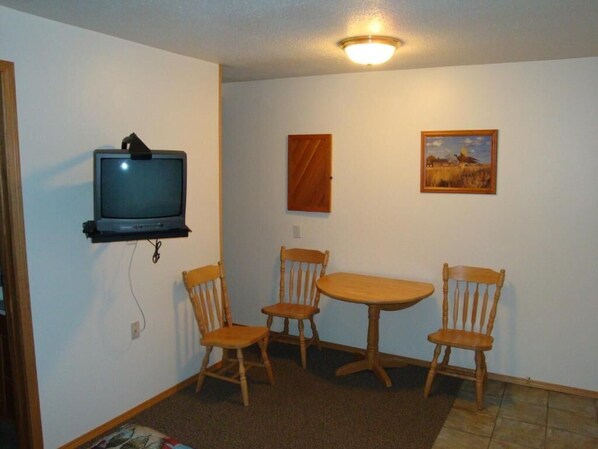 A small room with a television mounted on the wall, a wooden table, and four wooden chairs. - Motel Tyrol (Radium Hot Springs)