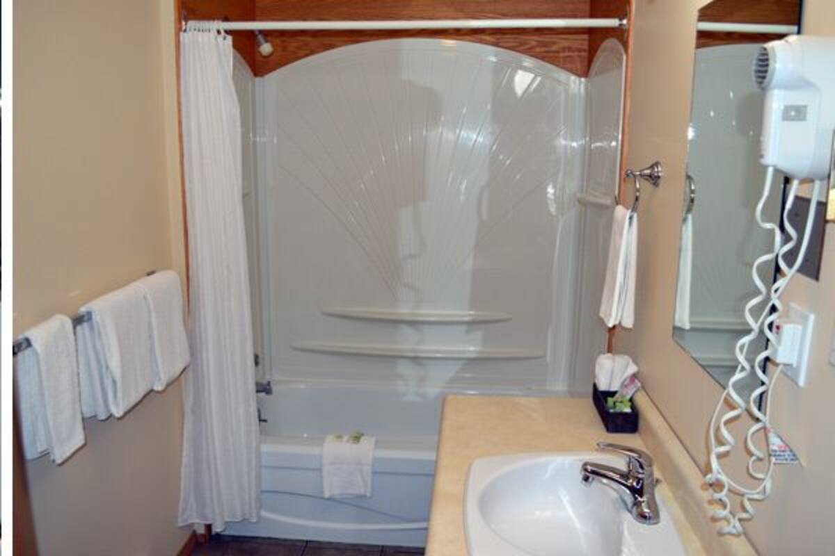 Eine kompakte Küche mit Kühlschrank, Mikrowelle und Holztisch. Außerdem Dusche mit Glastür sowie Waschbecken und Fön.