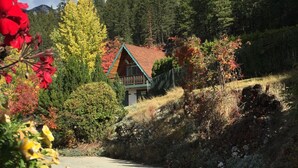 A rustic cabin with a red roof, surrounded by autumn foliage and a mountainous backdrop. - Motel Tyrol (Radium Hot Springs)