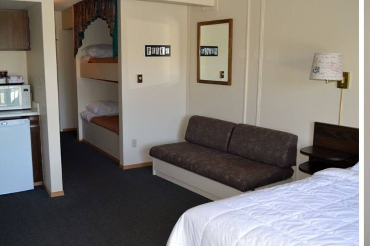 Ein Hotelzimmer mit Stockbetten, einer Couch, einem Schreibtisch mit Lampe und einer kleinen Küchenzeile.