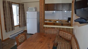 A compact kitchen with a microwave, refrigerator, and wooden cabinets. There is a dining table with chairs and a television mounted on the wall. - Motel Tyrol (Radium Hot Springs)