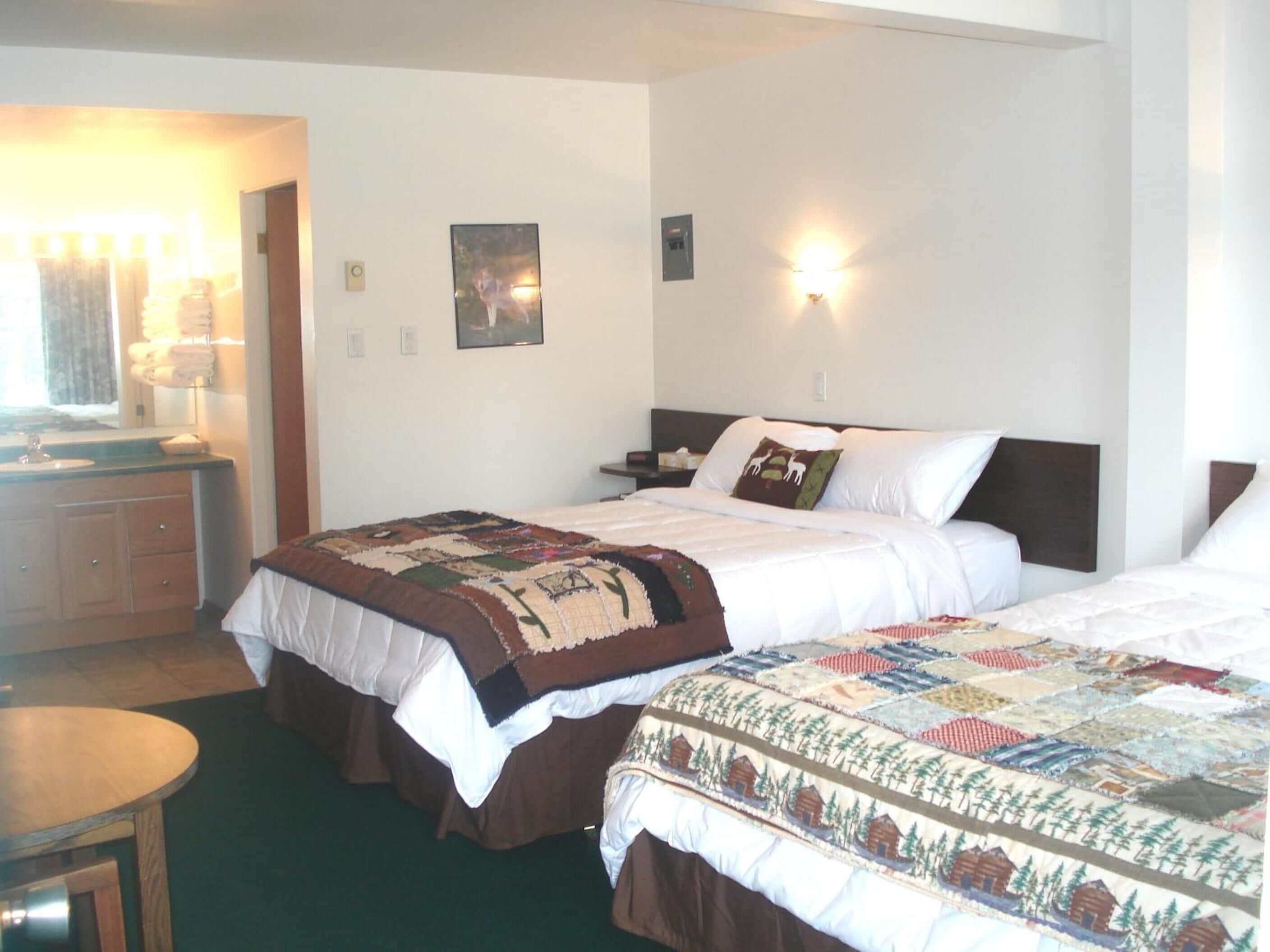 Une chambre d’hôtel avec deux lits, une petite table, une commode et une fenêtre avec des rideaux.