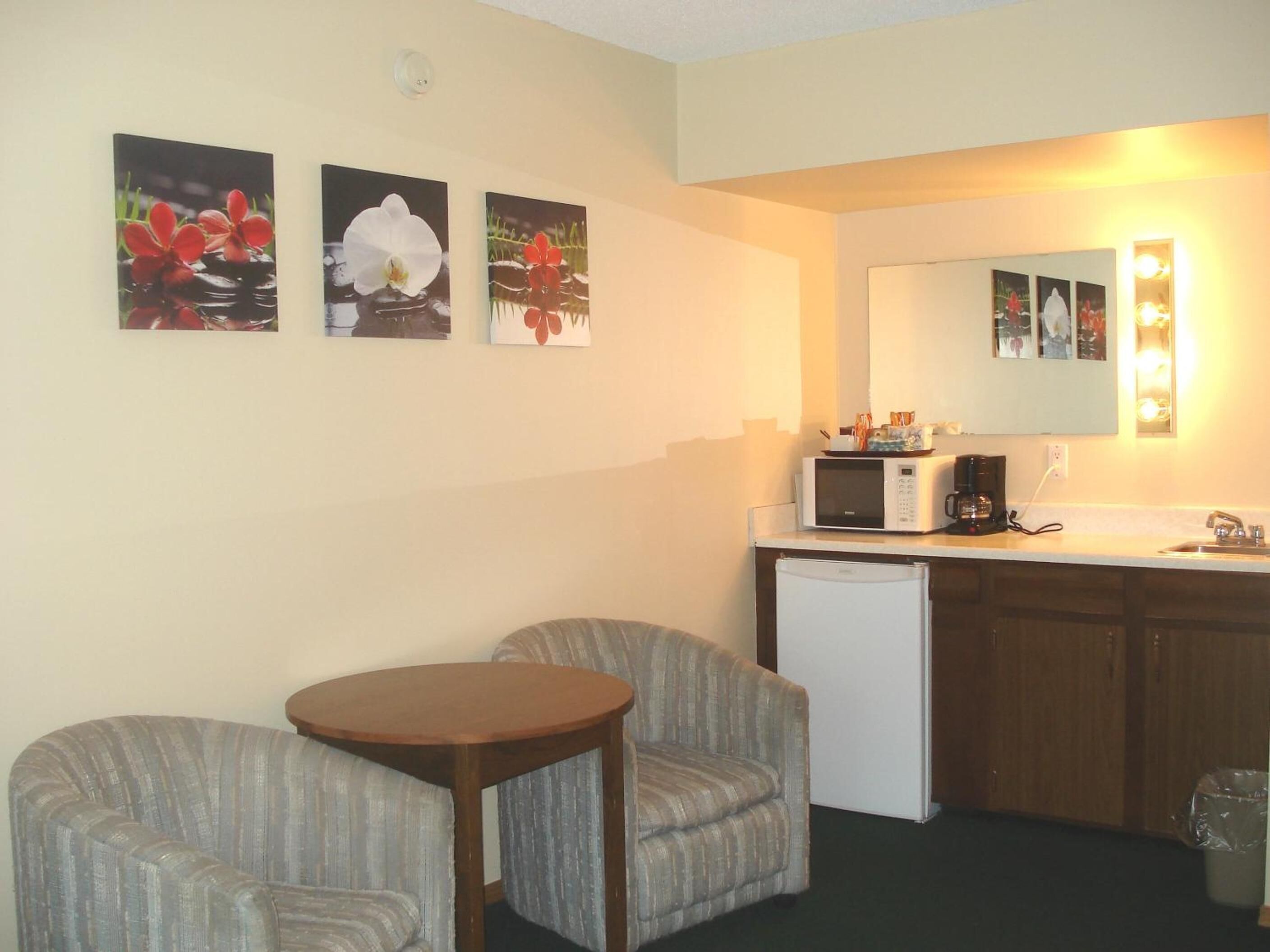 A compact living space with a kitchenette, two armchairs, a small wooden table, and wall-mounted artwork.