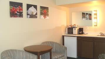A compact living space with a kitchenette, two armchairs, a small wooden table, and wall-mounted artwork.