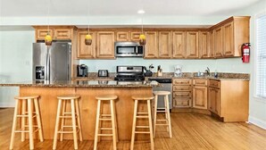 Una cocina con armarios de madera, un refrigerador de acero inoxidable, un microondas, una estufa y un lavabo. Hay cuatro taburetes de madera en la isla.