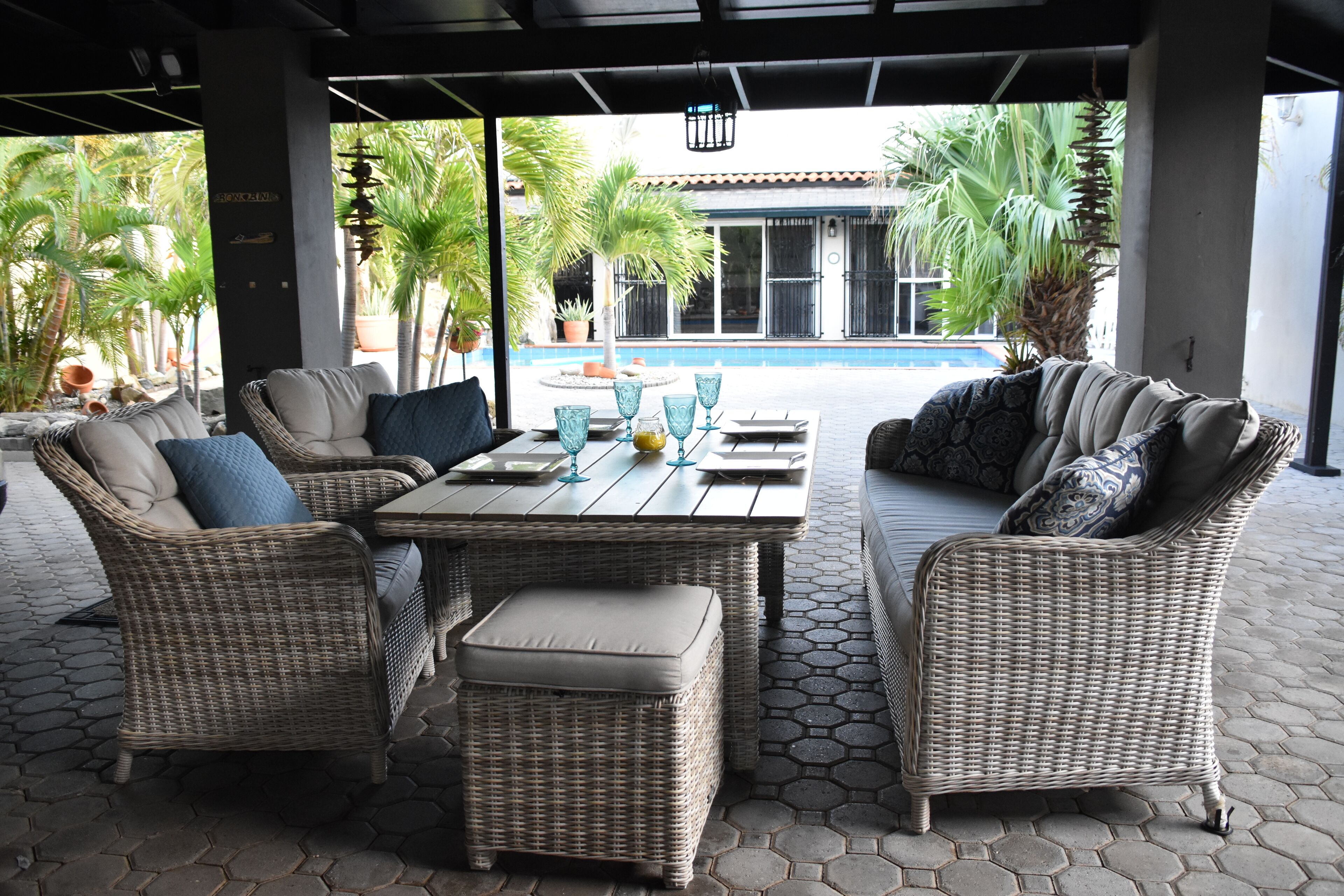 A covered outdoor seating area with wicker furniture and a pool in the background.