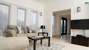 Una sala de estar con sofá, mesa de centro y televisor. Hay una puerta que da a otra habitación.