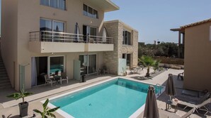 A two-story building with a swimming pool, outdoor seating, and a stone facade. - Michalianna suites (Hersonissos)