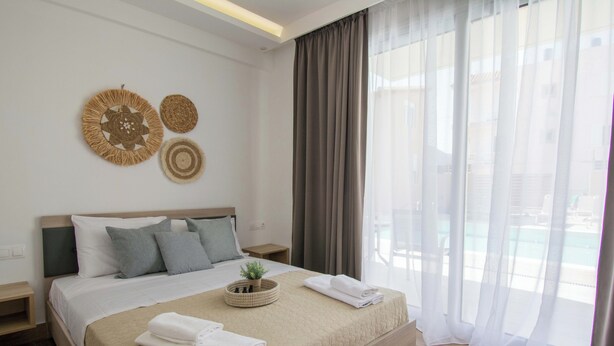 A neatly made bed with a beige quilt, pillows, and a small plant in a woven basket. - Michalianna suites (Hersonissos)