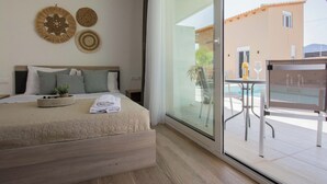 A bedroom with a bed, a small table with a plant, and a view of an outdoor pool area. - Michalianna suites (Hersonissos)