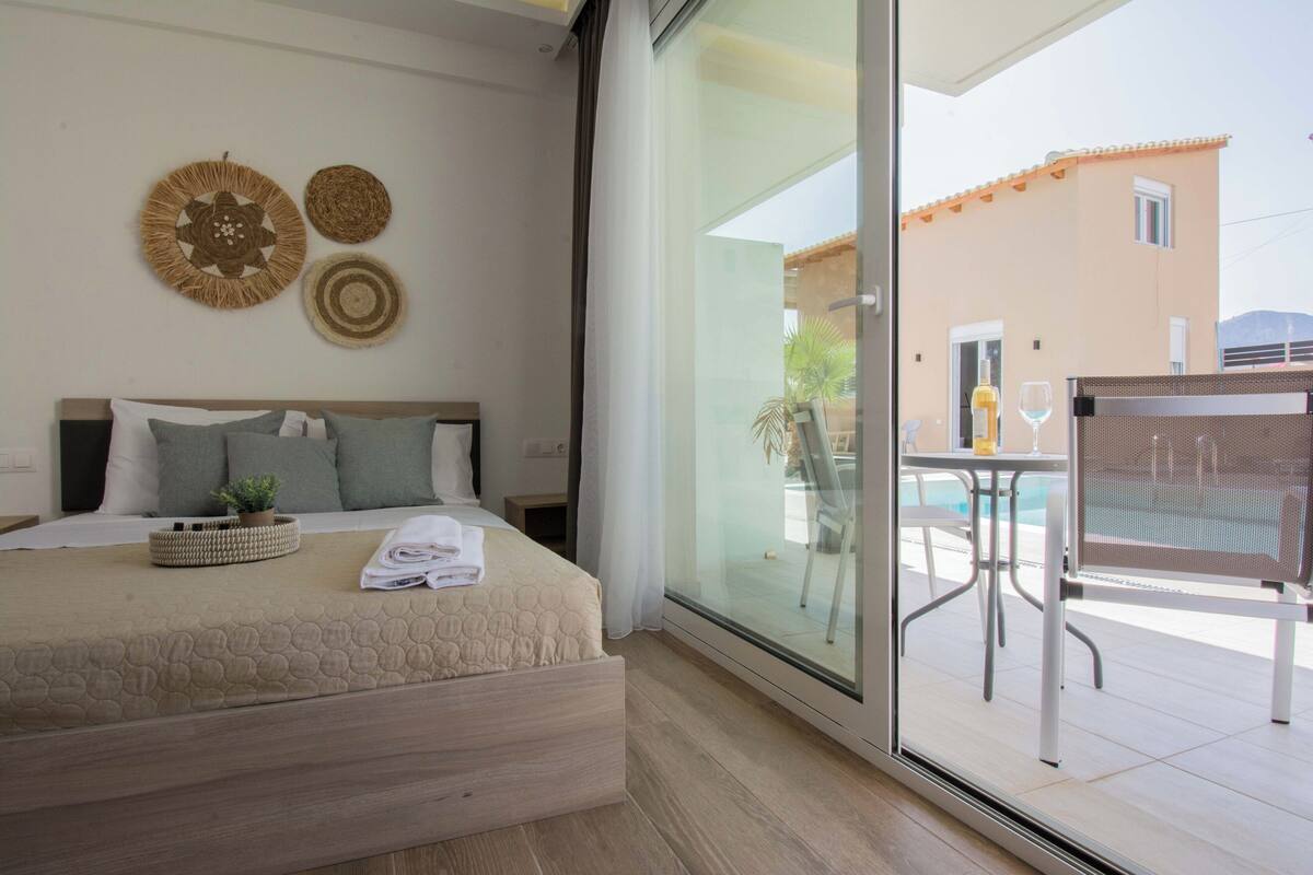 A bedroom with a bed, a small table with a plant, and a view of an outdoor pool area.