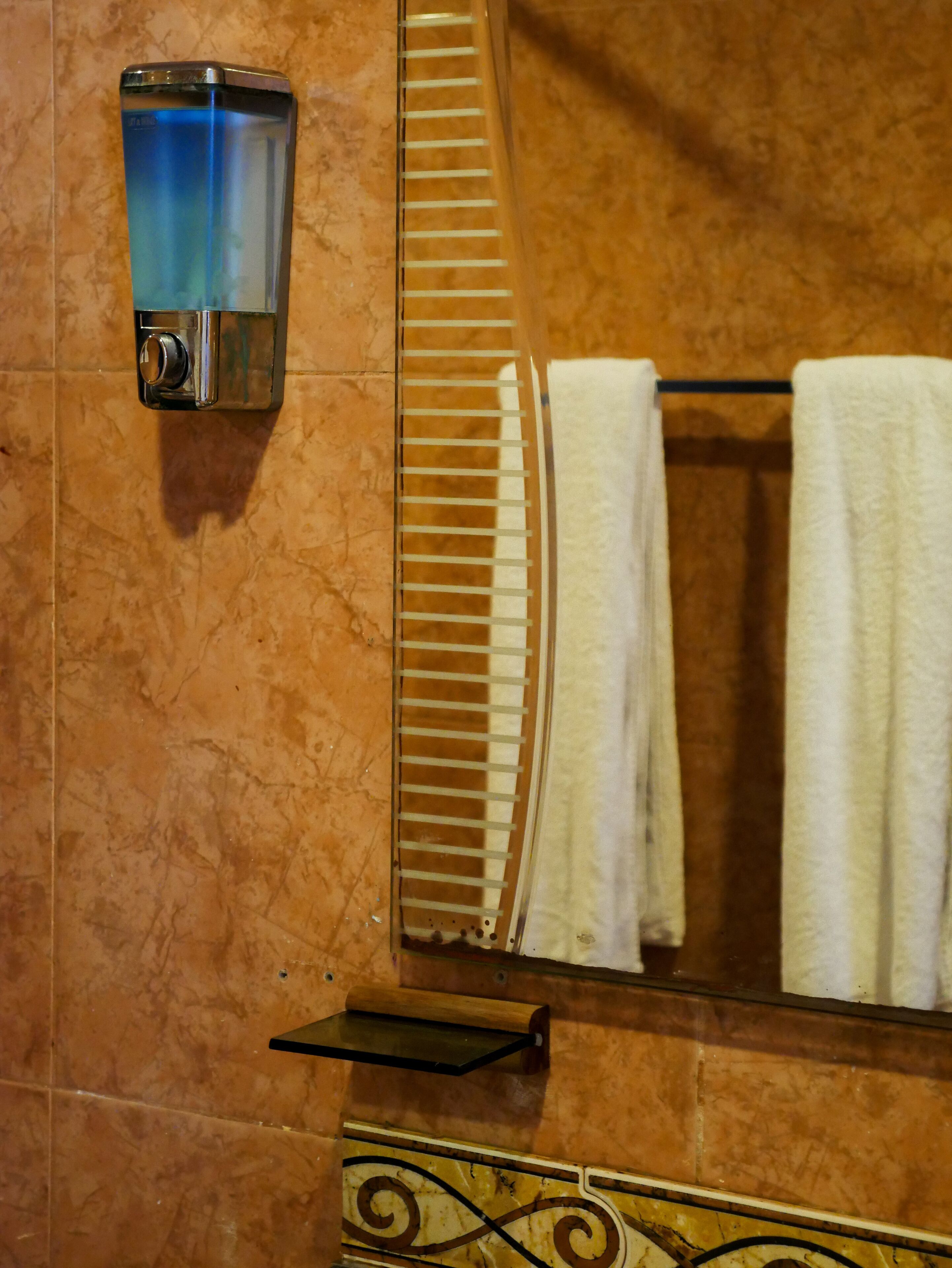 Un baño con pared de mármol, un perchero con toallas blancas y un dispensador de jabón.