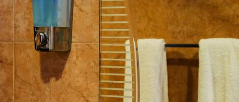 Un baño con pared de mármol, un perchero con toallas blancas y un dispensador de jabón.