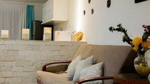 Ein Wohnzimmer mit Steinwand, einer Couch mit Kissen, einem kleinen Tisch mit Blumenvase und einer Küchenzeile im Hintergrund.
