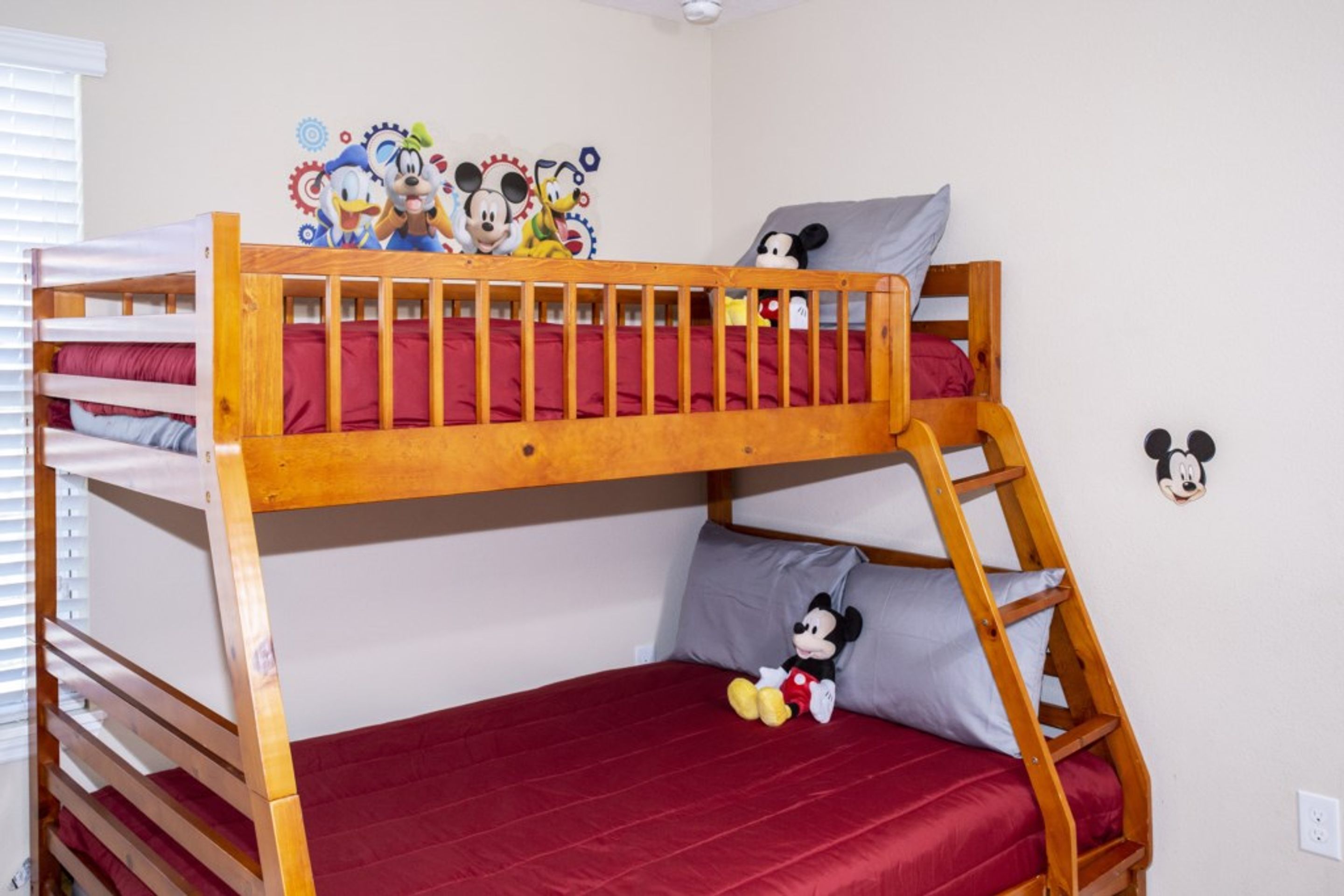 Uma cama box com um colchão vermelho, um bichinho de pelúcia do Mickey Mouse na cama de baixo e um adesivo de parede do Mickey Mouse.