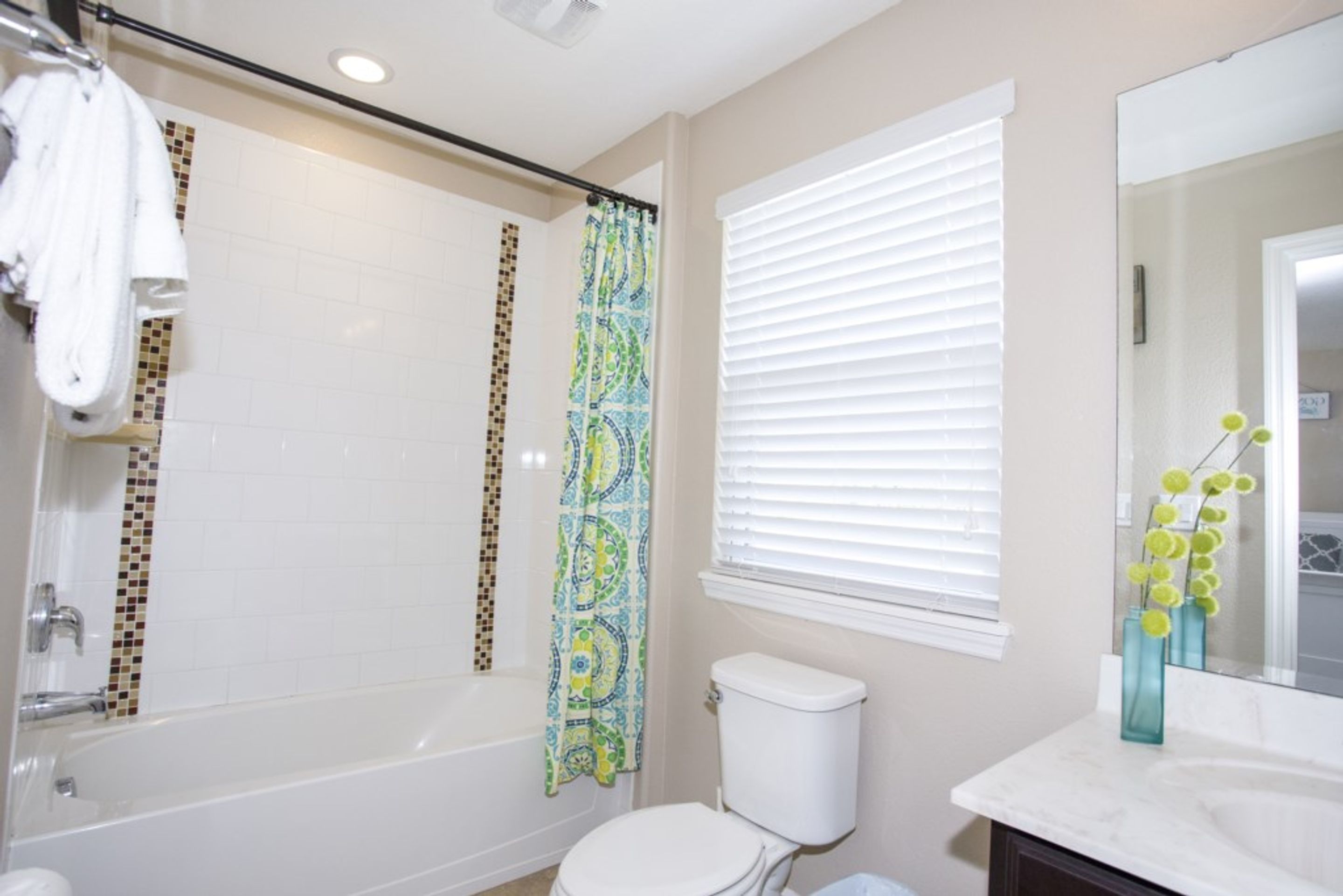 A bathroom with a bathtub, toilet, and a window with blinds.