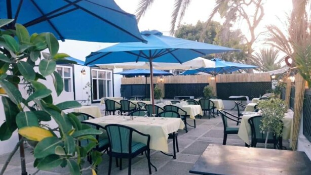 Un espace ext érieur aménagé en terrasse, avec des tables et des chaises, protégé par des parasols bleus et entouré de verdure.