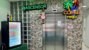 A hotel lobby with a Coca-Cola refrigerator, a neon sign for 'ASCENSOR' and 'COFFEE MATES', and a stone wall. - Hotel Plateros (Cusco)