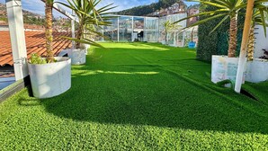 A well-maintained garden with artificial grass, potted plants, and a glass greenhouse structure. - Hotel Plateros (Cusco)