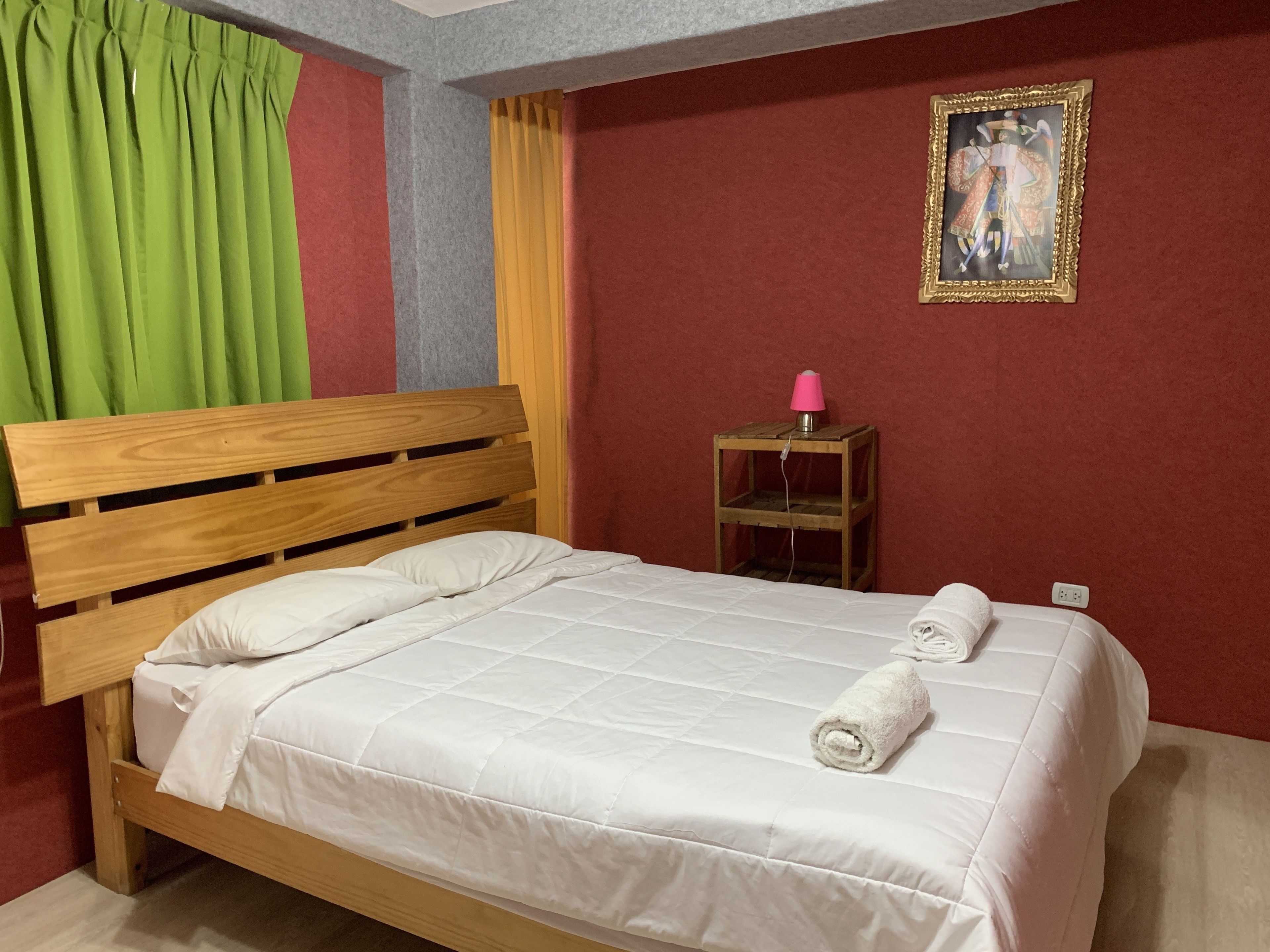 A neatly made bed with white bedding, a wooden headboard, and a green curtain to the left.