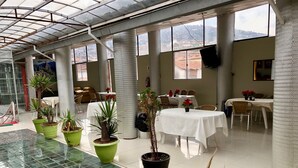 A spacious indoor area with a glass floor, green potted plants, and tables set for dining. - Hotel Plateros (Cusco)