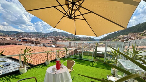 A terrace with a table and chairs, a yellow umbrella, and potted plants. - Hotel Plateros (Cusco)